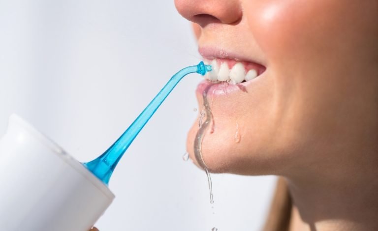 Wanita menggunakan water flosser untuk menghilangkan sisa makanan dan plak di antara gigi.