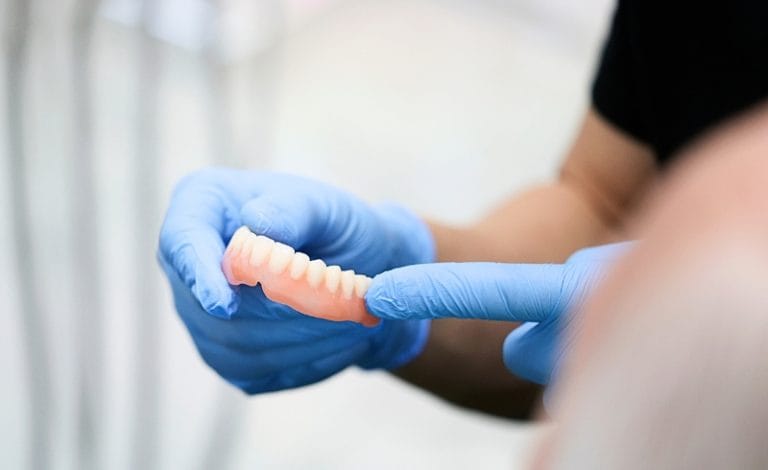 Dokter sedang memegang gigi palsu bagian bawah