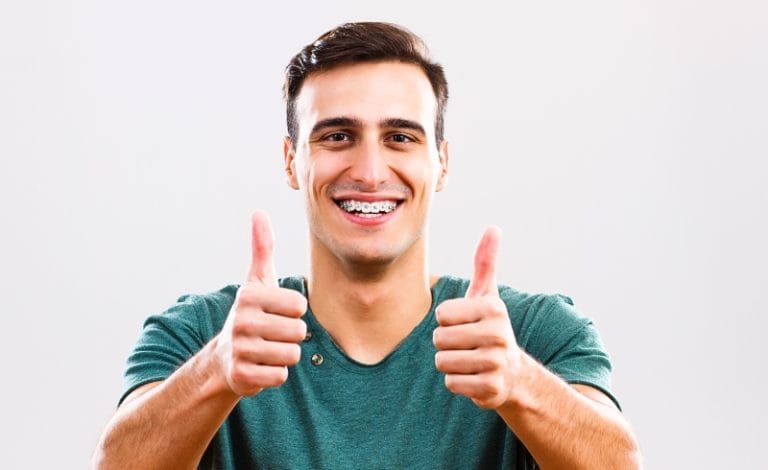 Pria berbaju hijau menggunakan karet behel warna hitam, salah satu rekomendasi warna karet behel untuk pria